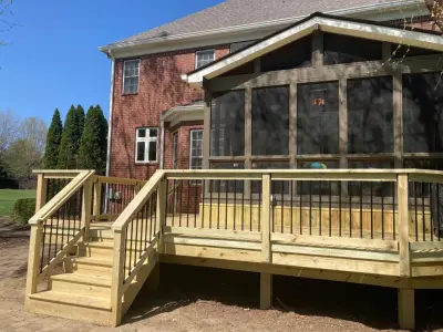 Deck with pressure-treated wood and black aluminum railings adjacent to existing screened room by Nixon Renovations