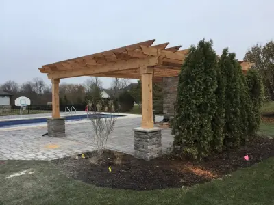 Spacious cedar pergola featuring wrapped stone columns — Deck Building & Repair project by DeckThisOut
